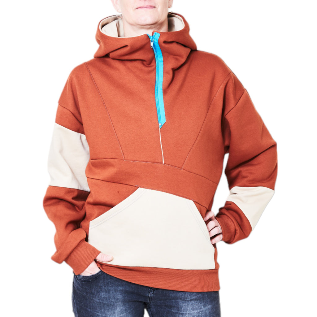 Kapuzenpullover in hennarot mit hohem Kragen. Kapuze innen in sandfarbem. Reißverschluss an der Kapuze in cyanblau. Asymmetrischen Hamstertasche vorn. An den Ärmeln und hinten je ein asymmetrischer Streifen in Sandfarbe.